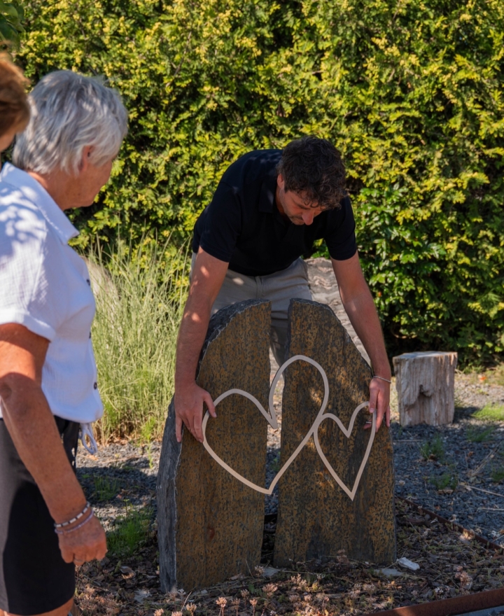Adviseur van Hutting Natuursteen toont een hartornament aan twee klanten in de monumententuin
