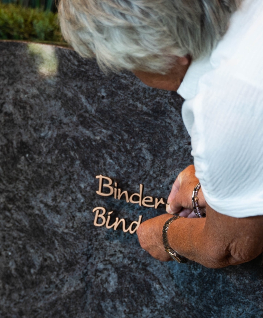Handen brengen bronzen letters aan op een geplaatst grafmonument